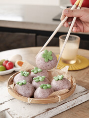 Purple Steamed Buns with Green Clover Decorations Being Picked Up with Chopsticks from Bamboo Steamer