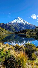 Snowy mountain peak reflects in tranquil lake, lush green surrounds