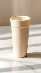 Off-white, cylindrical cup sits on a marble surface, illuminated by sunlight casting shadows