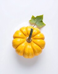 Overhead view of a small, yellow pumpkin with a green leaf