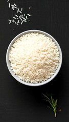 Overhead view of cooked white rice in a bowl, with grains and herbs nearby