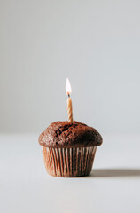 A single chocolate muffin with a birthday candle on a white table against a white background