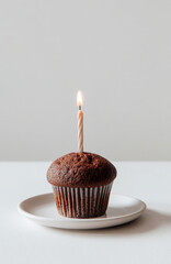 A single chocolate muffin with a birthday candle on a white table against a white background