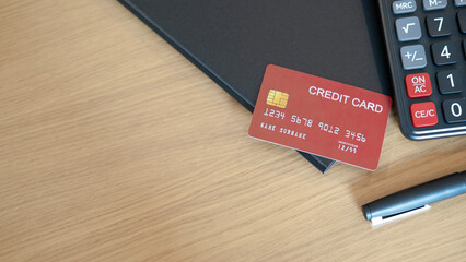 A red credit card placed on folder beside calculator and pen on wooden table representing consumer...