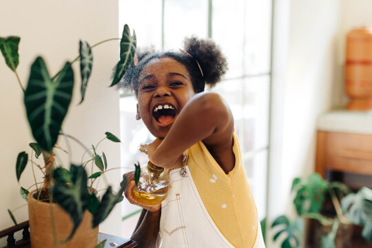 Excited girl spraying potted flowers in greenery-filled indoor garden - Powered by Adobe