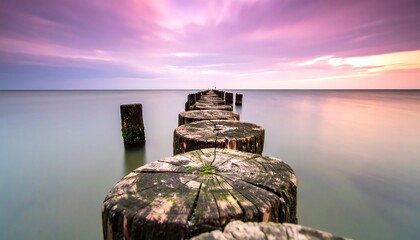 Wooden posts leading into the calm sea under a vibrant sunset sky.
