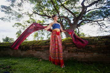 Traditional Thai dancer in colorful attire gracefully poses with flowing fabric in lush garden setting