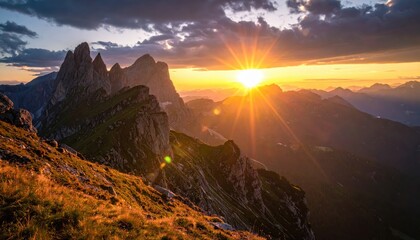 Brilliant golden sunset illuminates jagged mountain peaks and ranges in a stunning panoramic vista under a cloudy sky, creating a breathtaking natural landscape with warm and vibrant colors.