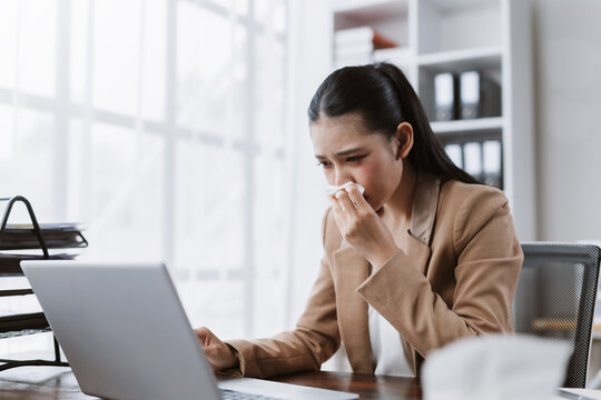 Asian businesswoman blowing nose at work office