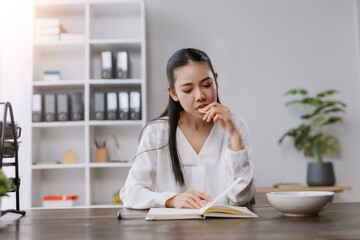 Asian woman reading book eating snack in office