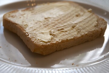 Close-up view of toasted bread slice spread with margarine on white plate.