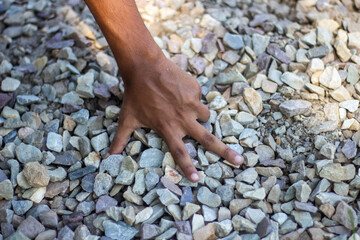 Hand sifting through a pile of small, rough stones