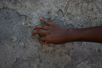 A hand touches a rough, textured stone wall with peeling paint