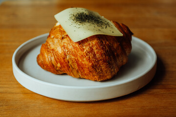 Fresh Baked Golden Croissant Topped with Cheese on White Plate Still Life