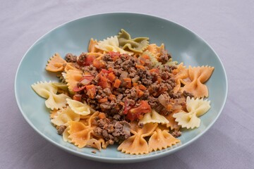 Italian cuisine close-up. Farfalle pasta with ground beef, tomato, onion and carrot ragù. Homemade cooked dish, authentic recipe, delicious comfort food background for culinary themes.