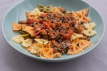 Italian cuisine close-up. Farfalle pasta with ground beef, tomato, onion and carrot ragù. Homemade cooked dish, authentic recipe, delicious comfort food background for culinary themes.