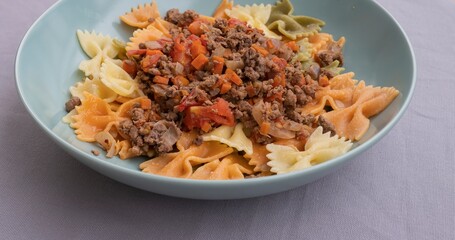 Italian cuisine close-up. Farfalle pasta with ground beef, tomato, onion and carrot ragù. Homemade cooked dish, authentic recipe, delicious comfort food background for culinary themes.