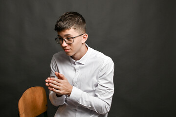 young man sits with hands rubbing together, gesture often expressing anticipation, anxiety, or inner tension in body language and psychology. Male rubbing hands, subconscious act, nervous excitement