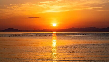 Dramatic Golden Sunset Over Calm Water with Mountain Silhouette and Reflective Glow in Sky
