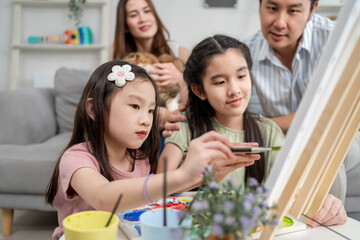 Asian young daughters enjoy painting on board with their parents at home. 