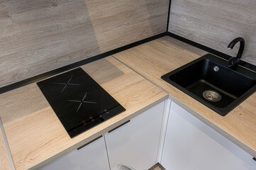 A modern kitchen corner featuring a sleek black induction cooktop, a black sink with matching...