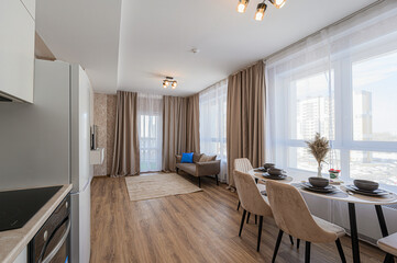 Cozy apartment with dining area set for four, a loveseat, and large windows. Neutral tones create a calming atmosphere with sheer and blackout curtains