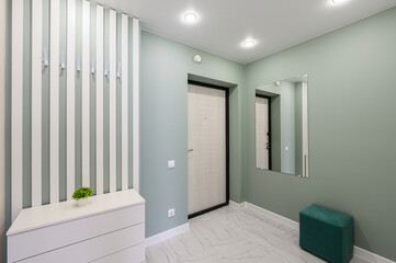 modern entryway with light green walls, white marble floors, and striped wall with hooks. white dresser stands below with small potted plant. mirror and green stool add to minimalist design