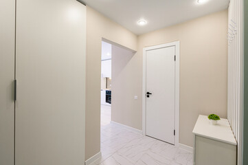 Bright hallway with a modern touch. Features beige walls, white marble floor, and a stylish white door with black hardware. Includes a glimpse into a white kitchen