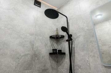 Modern shower with a black rainfall showerhead and handheld, set against a gray tiled wall....