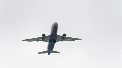 A perspective from below of a white commercial aircraft soaring through the air, its landing gear extended and the red engine pods visible, against a backdrop of a cloudy blue sky. High quality photo