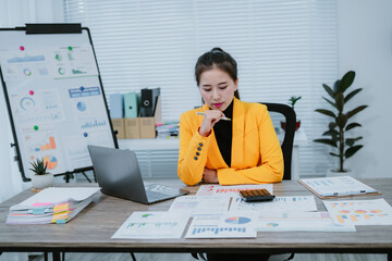 Young happy asian businesswoman in suit using tablet for video conference and holding smartphone, working with financial graphs and charts, sitting at desk in modern office
