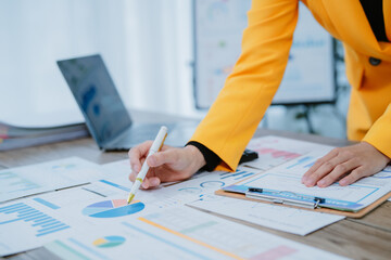 Asian professional woman working with a calculator at her desk, reviewing financial documents in a modern and well-lit office environment.