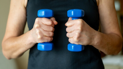 Faceless woman beyond fifty lifting blue dumbbells at home, consistent workout habit for healthy...
