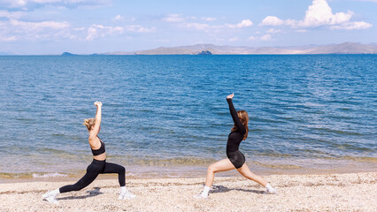 Women practicing yoga poses on a beach by the water in bright sunlight