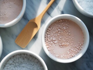 Overhead view of various natural clay powders in white bowls with a wooden scoop ready for beauty treatments.