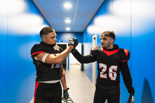 American football players in black and red uniforms giving a high five, showing teamwork and sportsmanship in a locker room