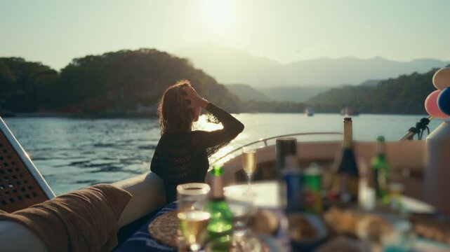 Romantic weekend, dinner on board of luxury yacht, celebrating anniversary. Pretty woman admiring amazing landscapes and scenery from pleasure boat, food and drinks on table, enjoy life and vacation