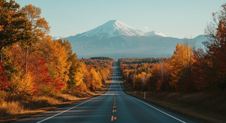 Open road leading towards snow capped mountain with vibrant autumn foliage on either side under clear sky