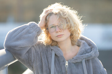 Young person posing with blonde hair and glasses