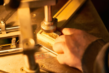 Man operating industrial machine with right hand adjusting metal component on workbench, focusing on precision manufacturing process in workshop setting
