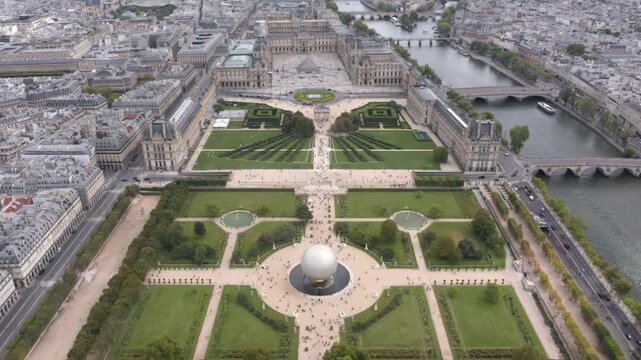 Aerial drone view rising over the Tuileries Garden capturing the Louvre with Pyramid, the Seine River, the Olympic Games cauldron ball and the historic city skyline stretching into the horizon.