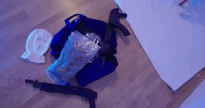 Dramatic setup with various props on a wooden floor, including a bag, mask, and objects arranged under blue lighting. Concept for thriller, crime story, or cinematic scene design.