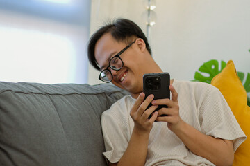 Cheerful Asian Down Syndrome Boy Enjoying Social Media on Smartphone While Relaxing at Home