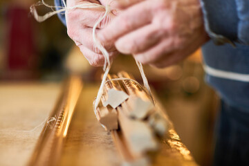 Man binding moldings with twine, hands working on carpentry project in workshop