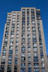 Fototapeta premium Modern residential high rise building with multiple glass windows and beige stone facade. Clean lines and architectural symmetry, showcasing urban living and contemporary cityscape design