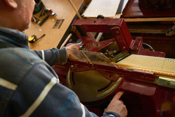 Man operating industrial cutting machine in workshop, hands adjusting equipment while working on precise measurement task, wooden materials visible on table