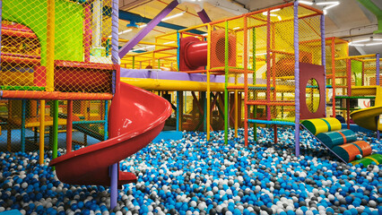 Colorful indoor playground with slides, climbing structures, and a ball pit full of blue, white, and black plastic balls, perfect for kids fun and birthday parties.