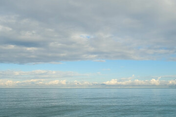 Cloudscape transforming over calm ocean waters with ripples on surface. Soft white cumulus clouds drifting above expansive blue sea waters, generating peaceful atmosphere with serene marine landscape.