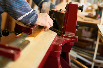 Man operating woodworking machine, hands adjusting wooden plank on industrial equipment in carpentry workshop, focusing on precision and craftsmanship