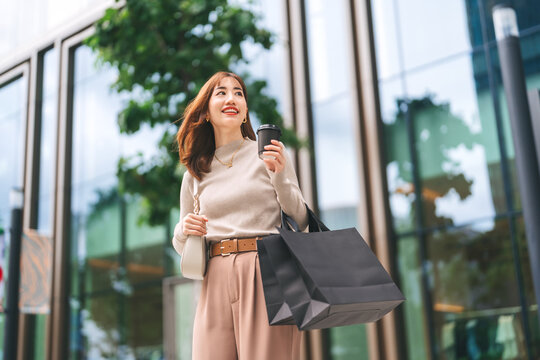 Single beautiful adult asian business woman holding take away coffee cup and black shopping bag - Powered by Adobe